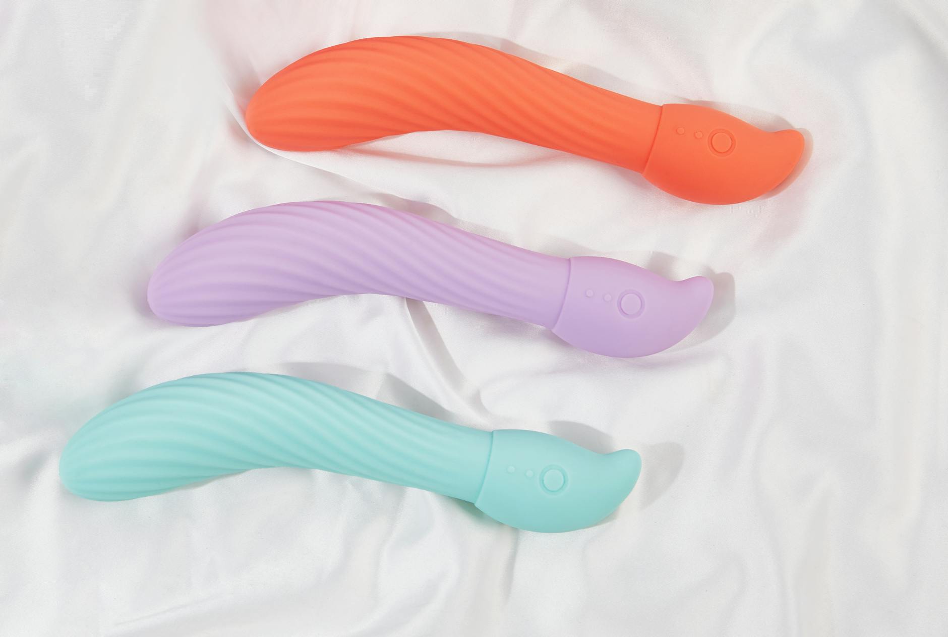 Three colorful clitoral vibrators arranged on white fabric, showing different vibrator designs including modern air-pulse technology