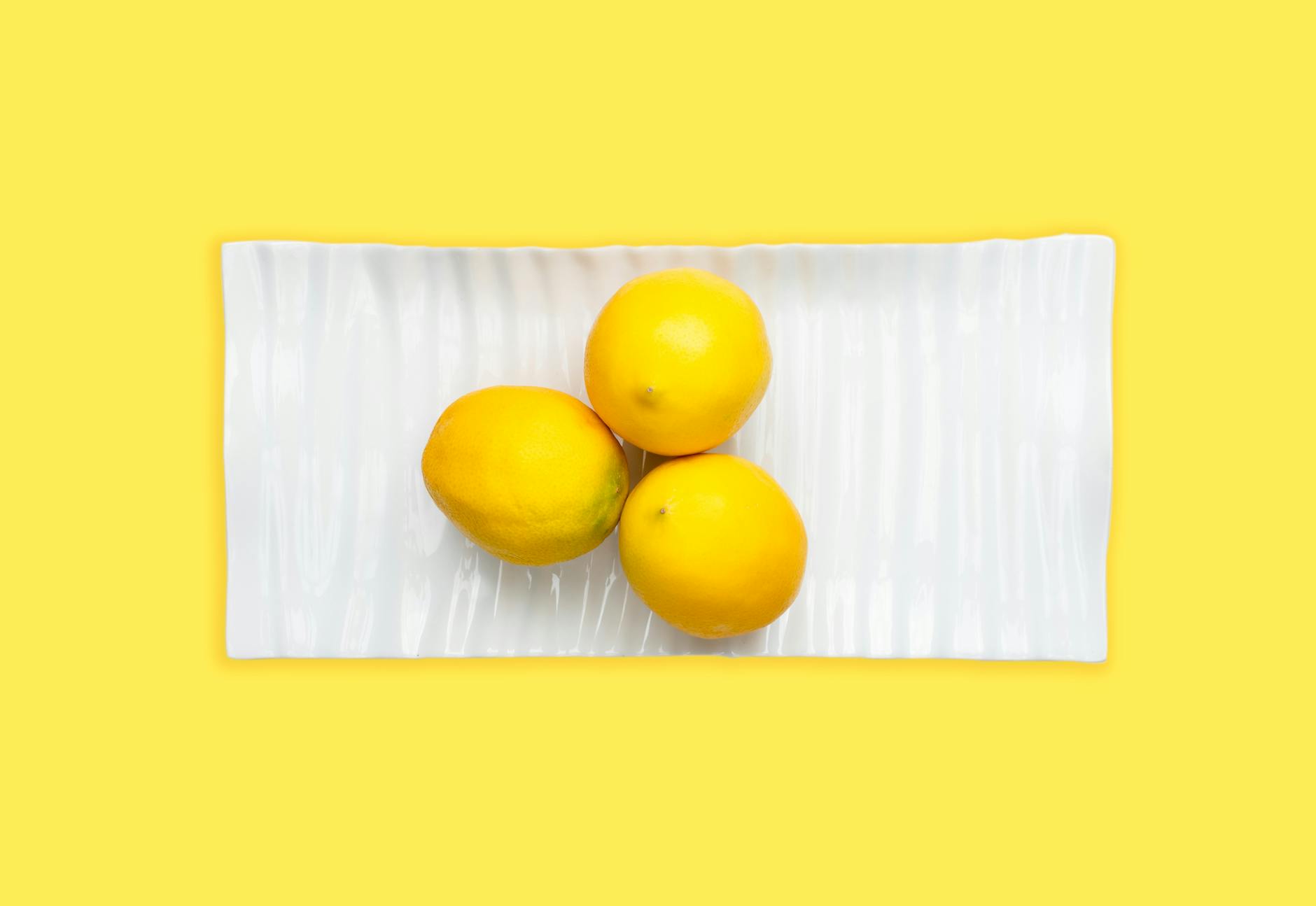 Fresh lemons arranged on white plate with bright yellow background