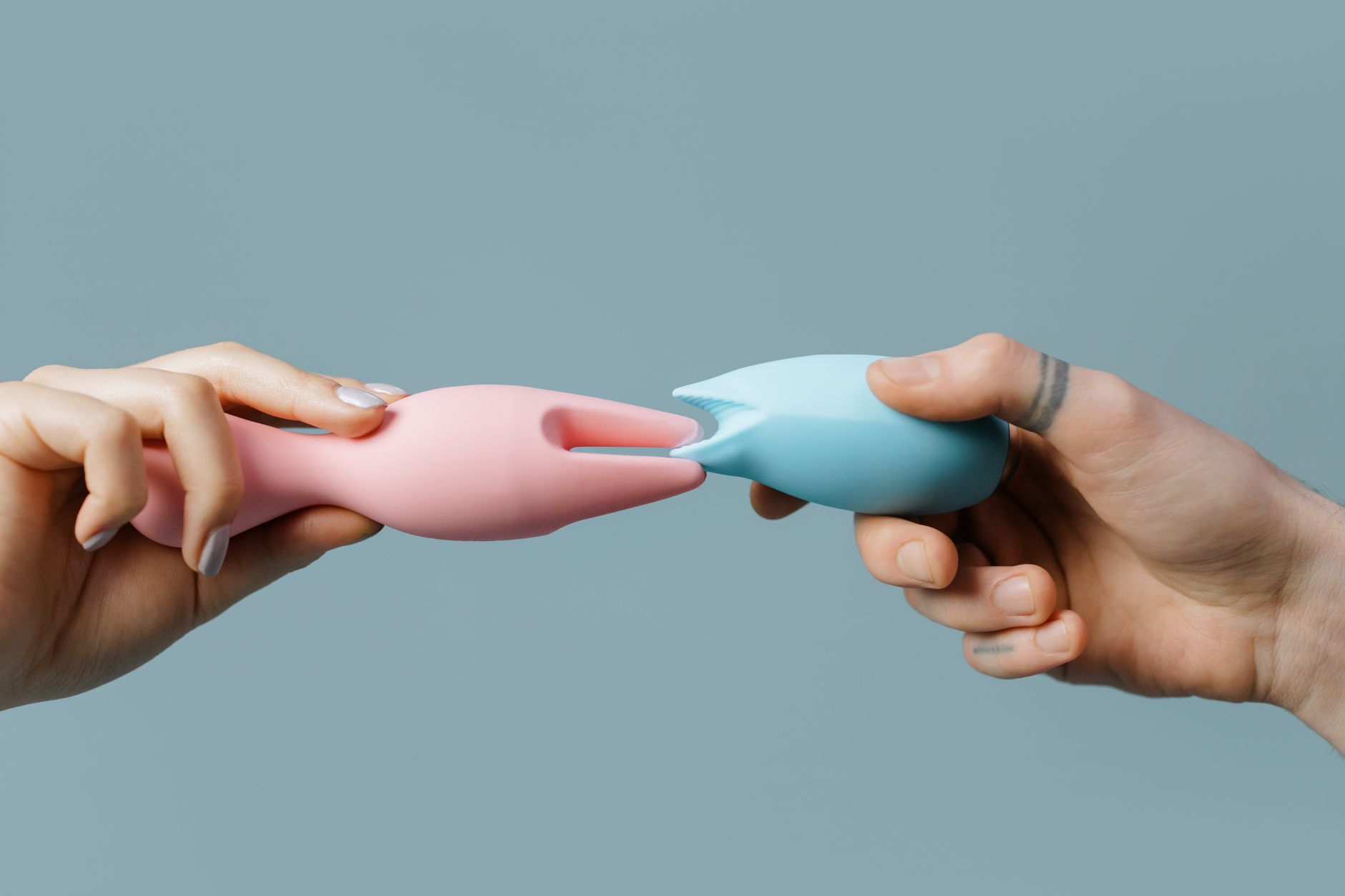 Blue silicone clitoral vibrator held in hand against purple background