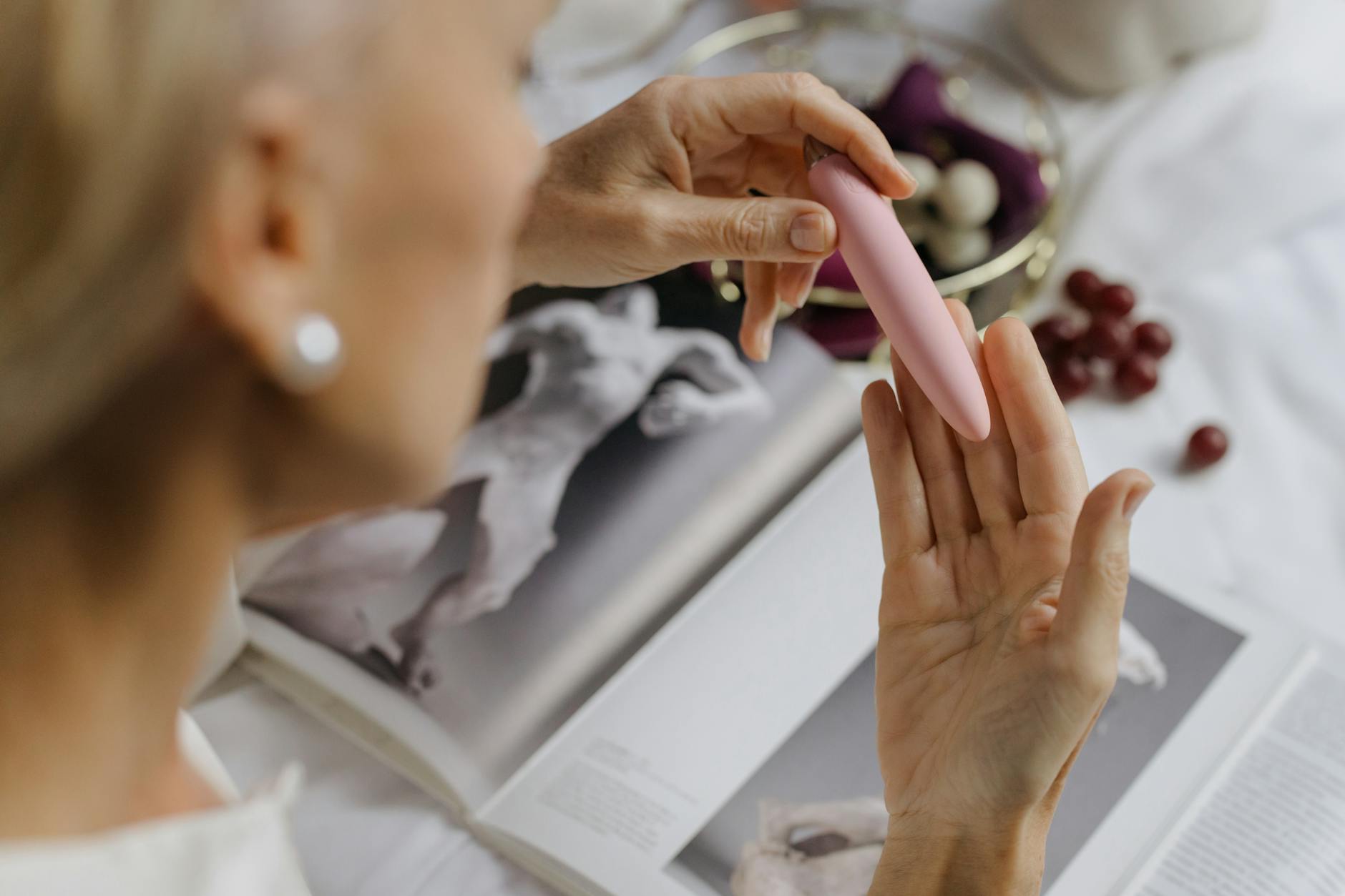 Mulher segurando vibrador rosa com livros de arte ao fundo, enfatizando temas íntimos e pessoais