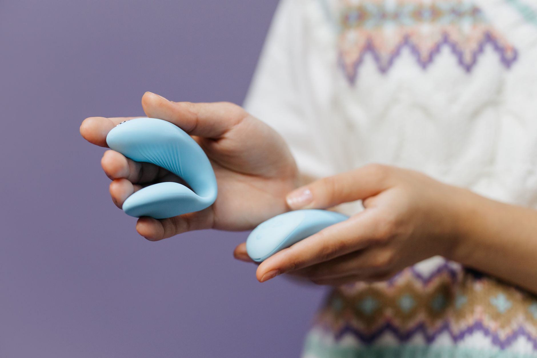 Close-up of hands holding a sleek blue vibrator against a purple background, representing pleasure reclamation during stress.