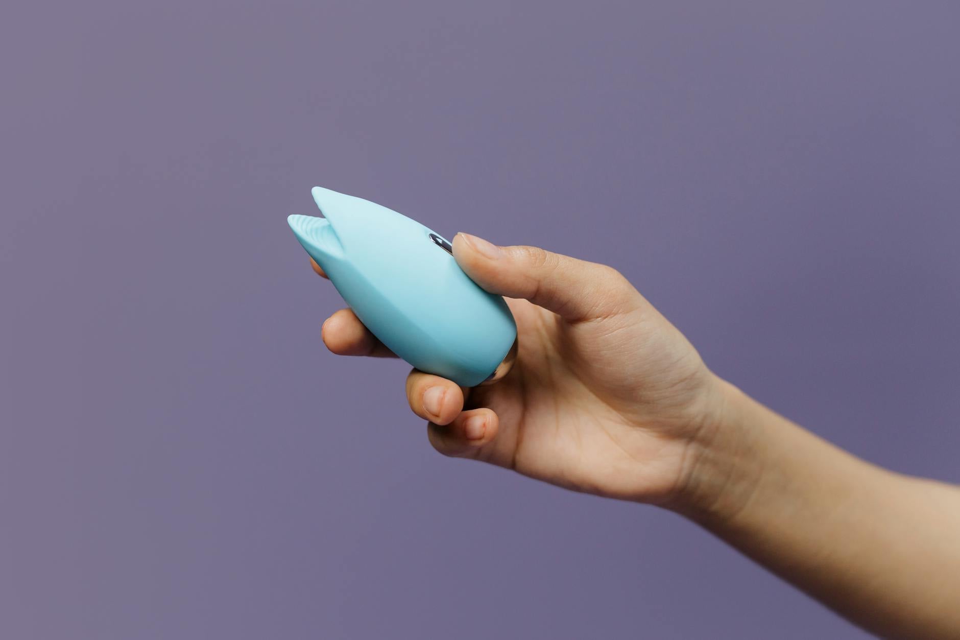A blue silicone sex toy held in hand against a purple background, representing pleasure and self-care while managing medication side effects.