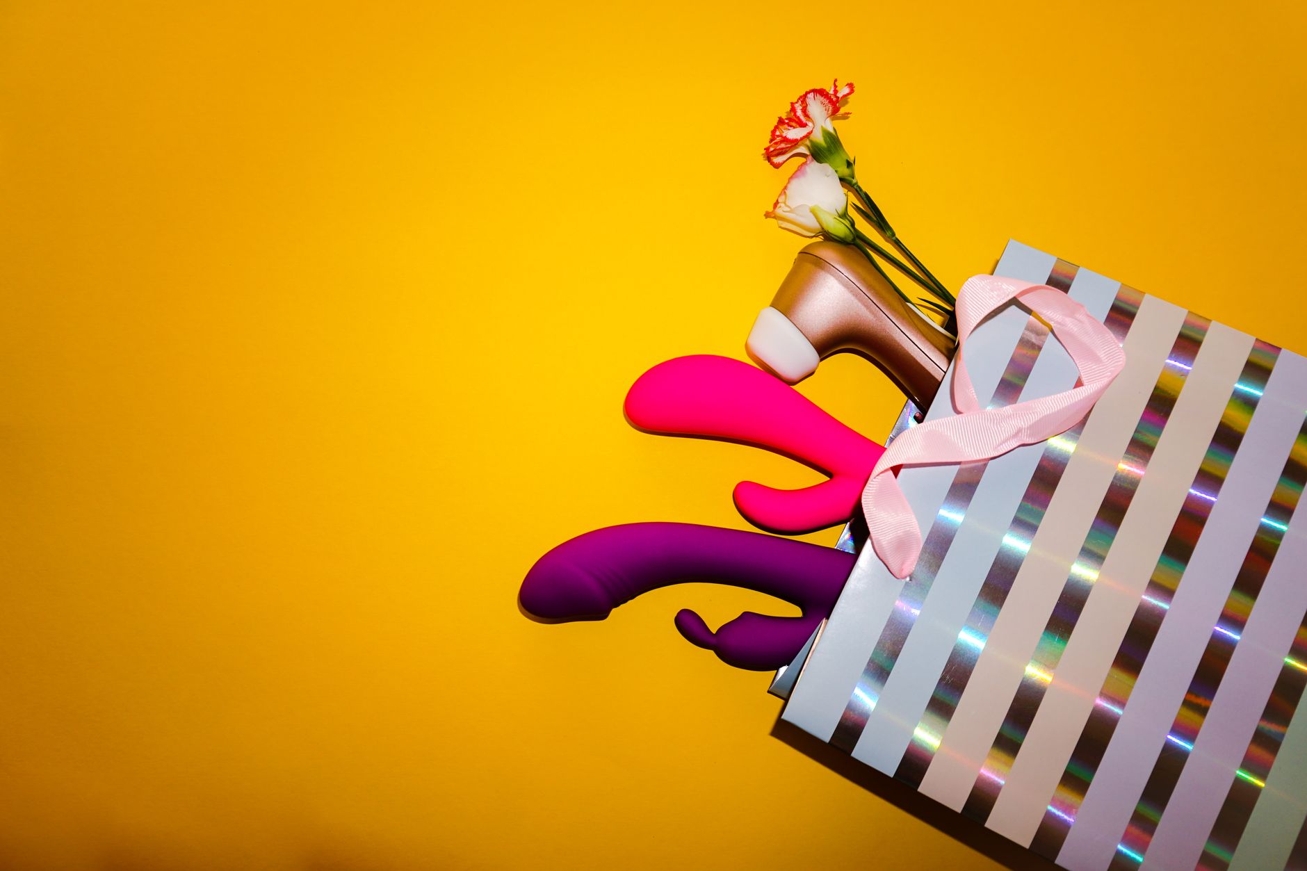Colorful vibrators with flowers displayed in a gift bag against a vibrant yellow background