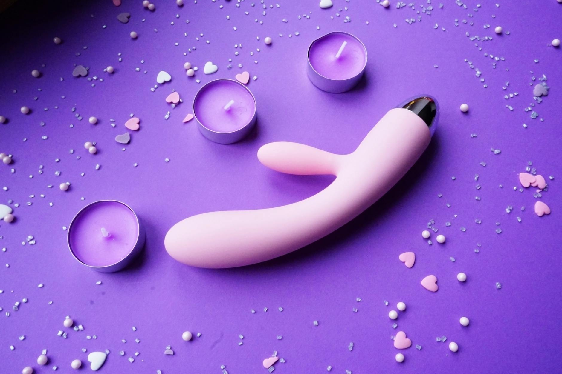 A hand holding a bright yellow lemon on a soft pink background, symbolizing the approachable design of lemon vibrators for beginners.